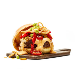 Loaded burger with melted cheese and roasted peppers on cutting board – restaurant photographer Toronto