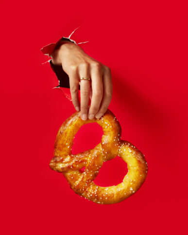 A hand holds a delicious pretzel against a bold red background. This simple yet striking social media image.